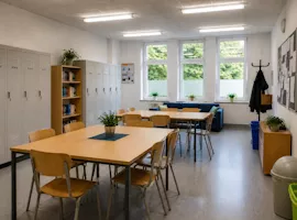 Freundlicher Aufenthaltsraum in einer Schule mit Tischen und Garderobe